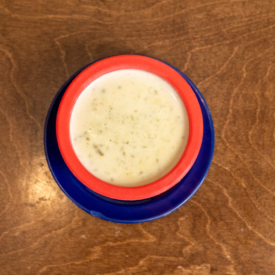 Bowl of creamy herb-speckled soup on a red-and-blue plate atop a wooden table.