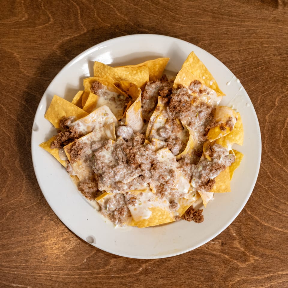Plate of tortilla chips topped with seasoned ground beef and melted cheese on a wooden table.