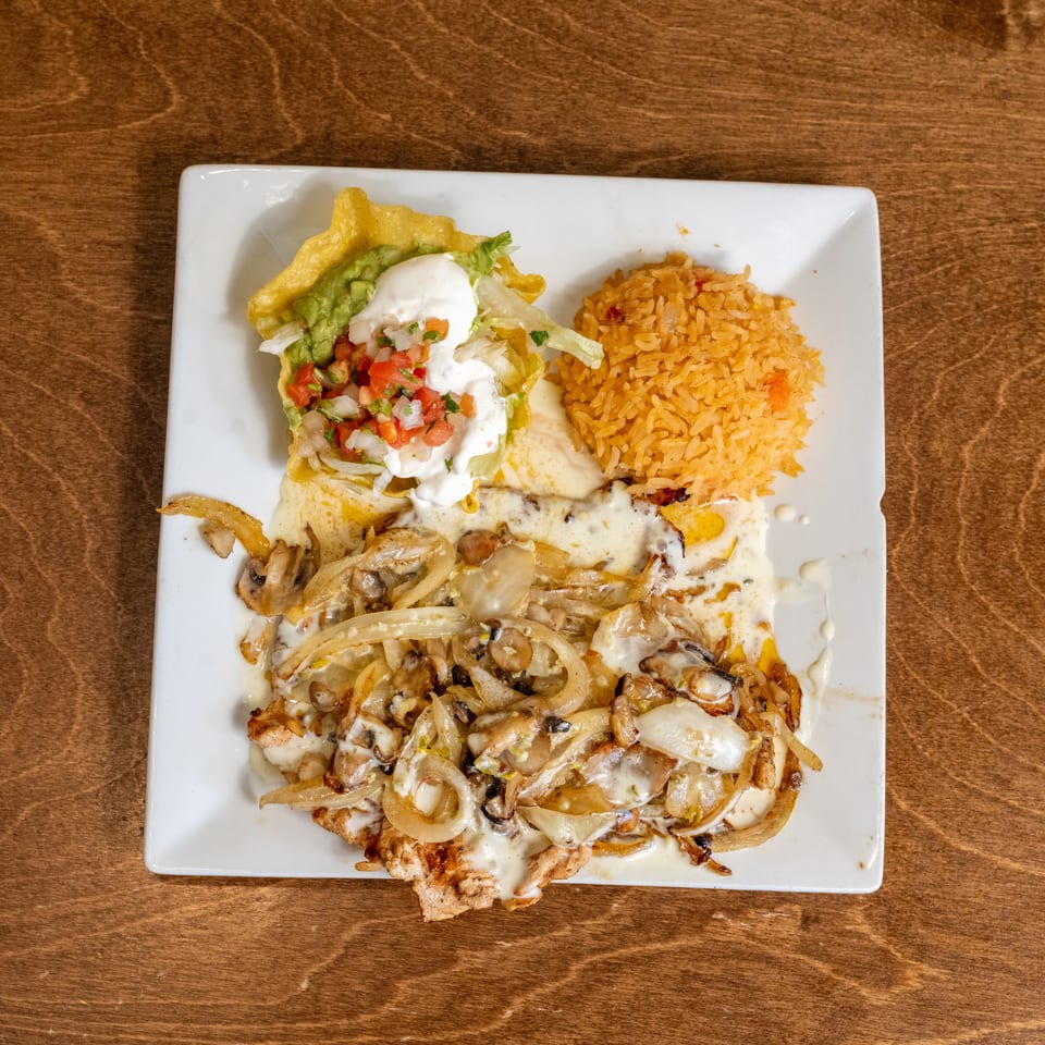 Mexican-style platter with grilled chicken, sautéed onions and mushrooms, creamy sauce, rice, guacamole, lettuce, pico de gallo, and sour cream.
