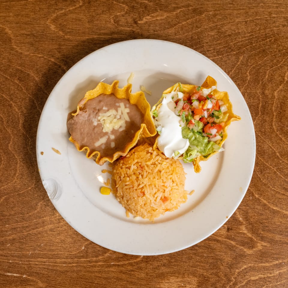 Mexican plate with refried beans, Spanish rice, and tortilla bowls filled with lettuce, guacamole, sour cream, and pico de gallo.