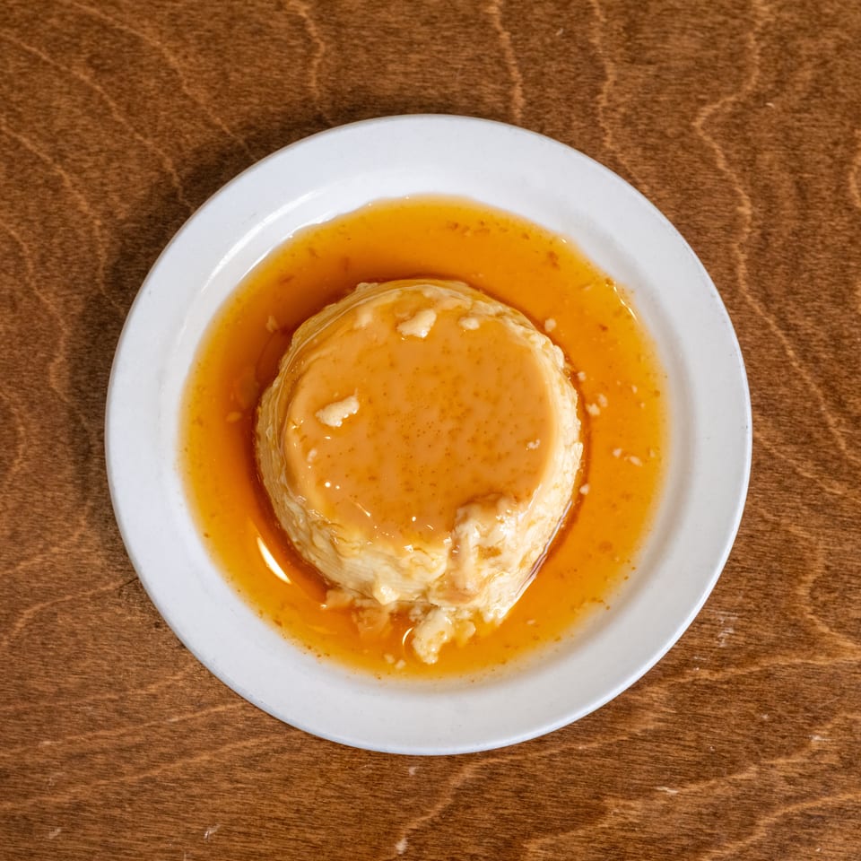 Caramel flan served on a white plate atop a wooden table.